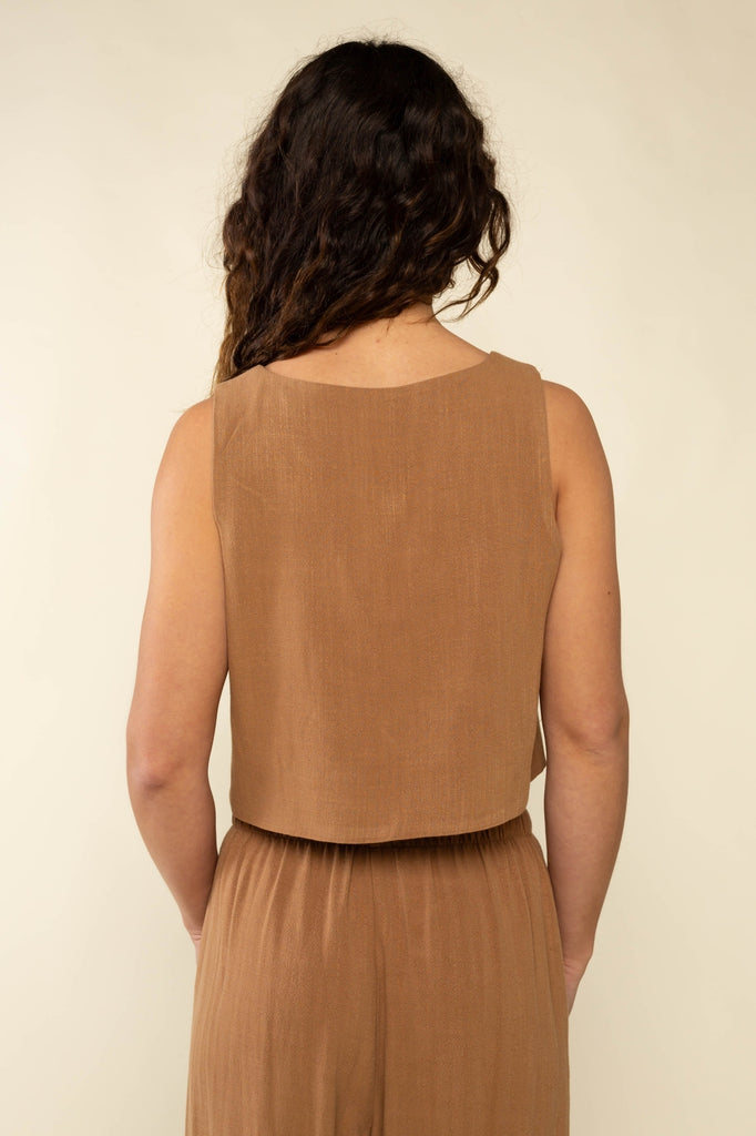 Woman wearing a brown sleeveless top and skirt set against a beige background