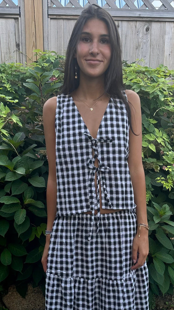Woman wearing a black and white checkered dress standing outdoors with greenery in the background