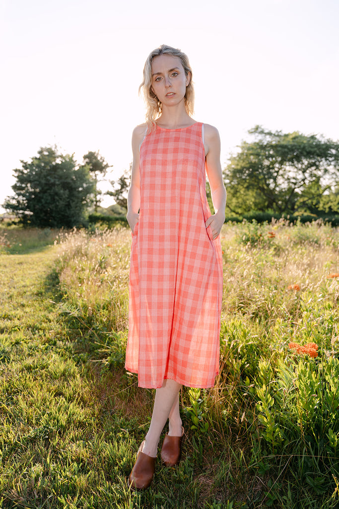 Woman in a pink checkered dress standing in a field with trees in the background
