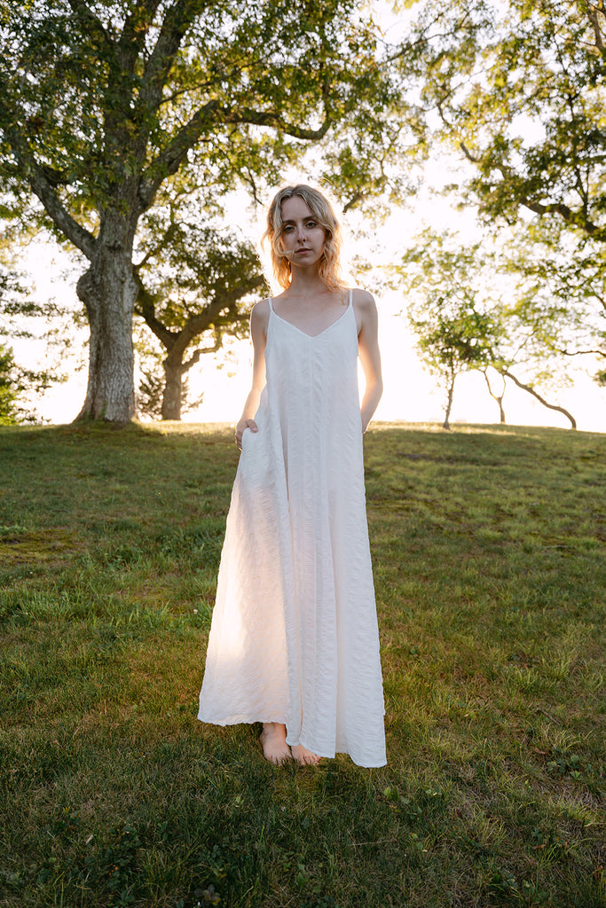 Woman in a white dress standing in a grassy field with trees in the background