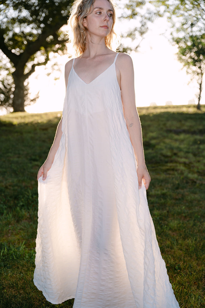 Woman in a white dress standing in a grassy field with trees in the background