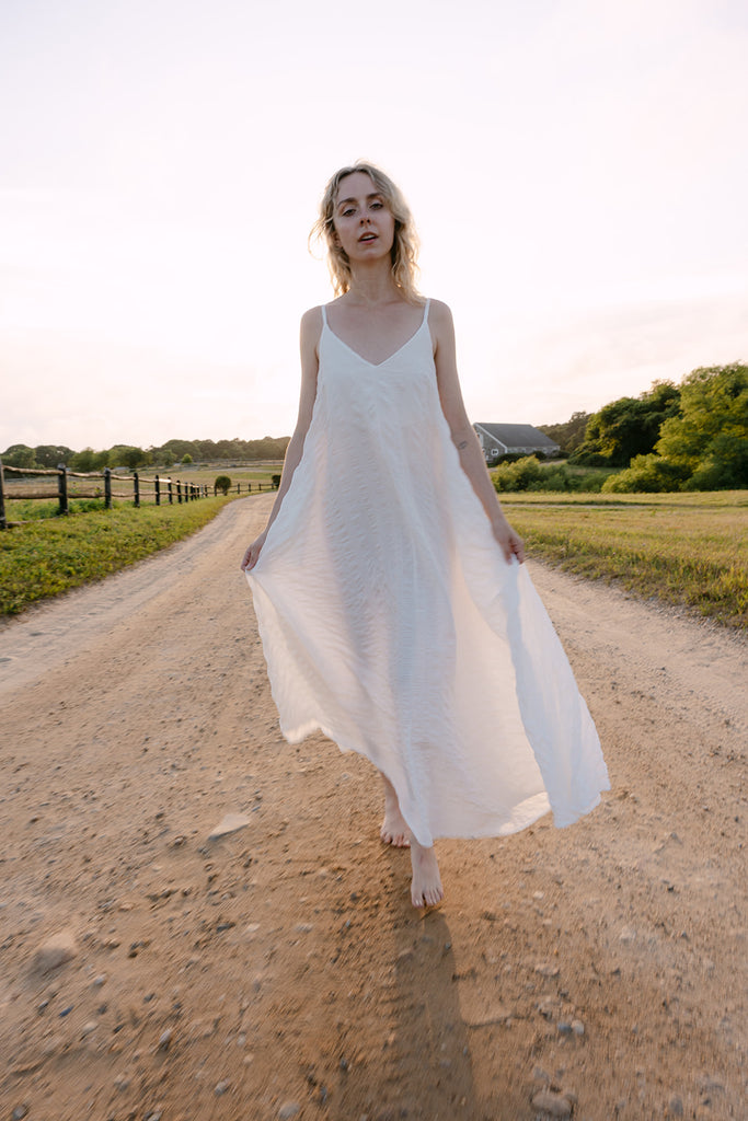Woman in a white dress standing on a dirt road with a scenic background